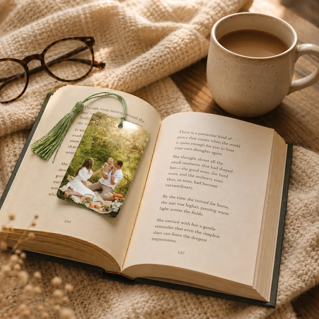 Personalised photo bookmark with tassel placed inside an open book beside coffee in a cosy reading setting