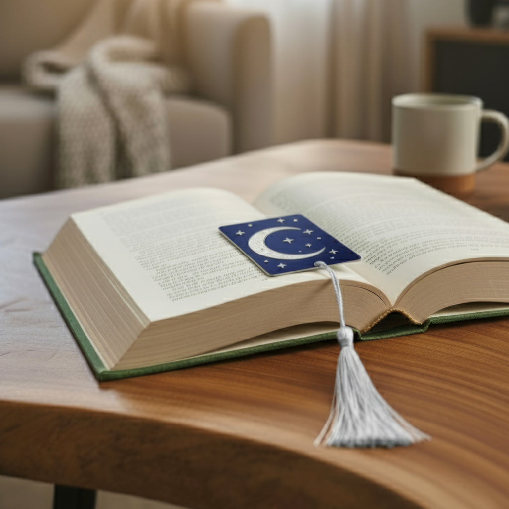 Personalised metal photo bookmark with white tassel resting on an open book – celestial moon and stars design printed on aluminium. Custom photo bookmark handmade in the UK, ideal gift for readers, book lovers and teachers.