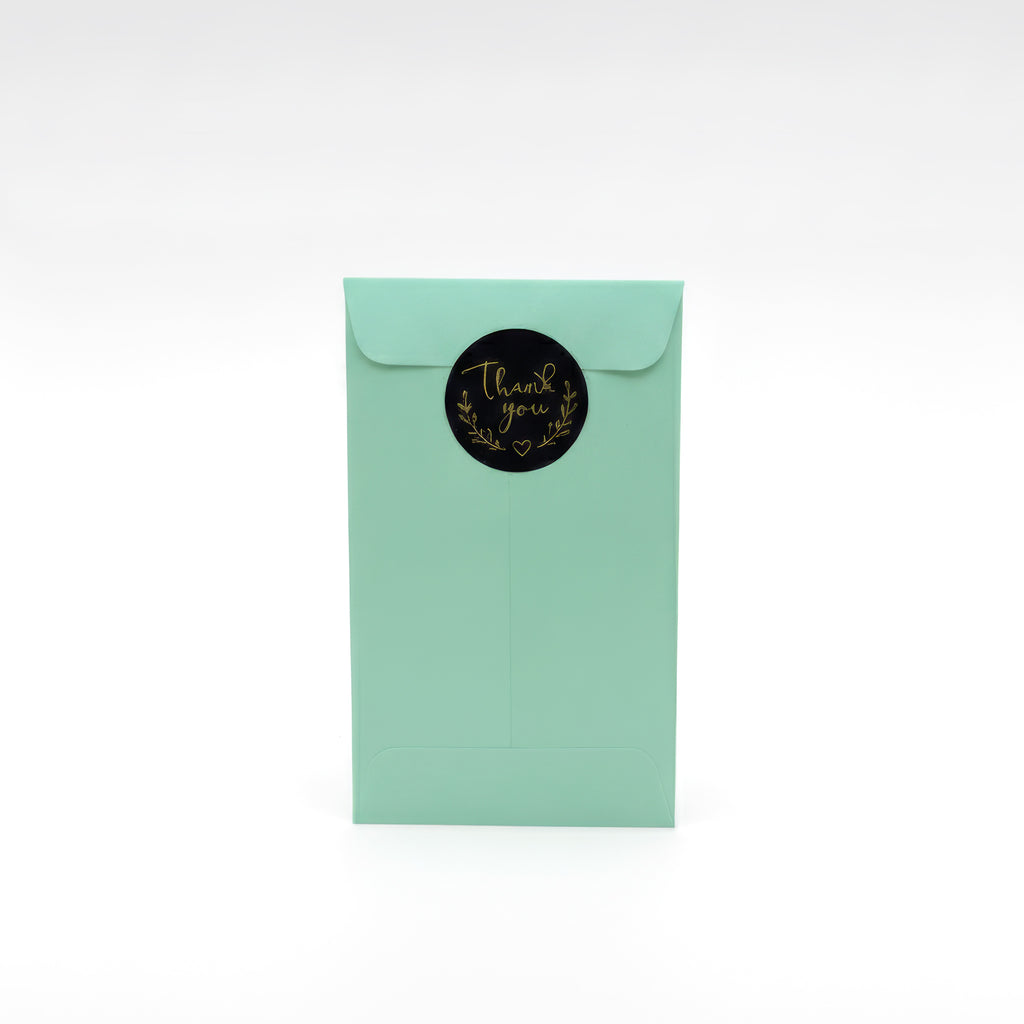 Mint green gift envelope with black and gold “thank you” sticker, presentation packaging for personalised flower bookmarks from PrintPhotos UK.