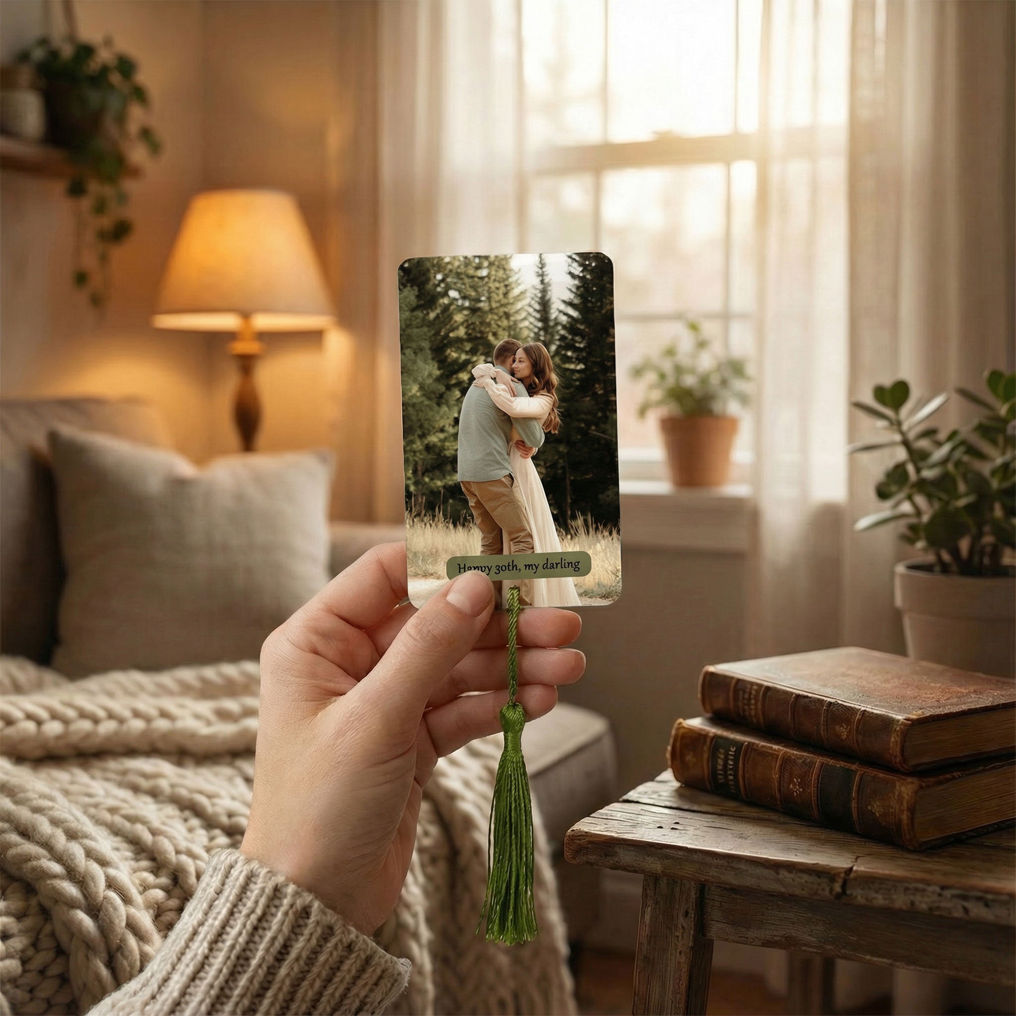 Hand holding a custom metal photo bookmark to show credit card size and print quality. Durable aluminium keepsake featuring a couple's photo, held against a cosy living room background.
