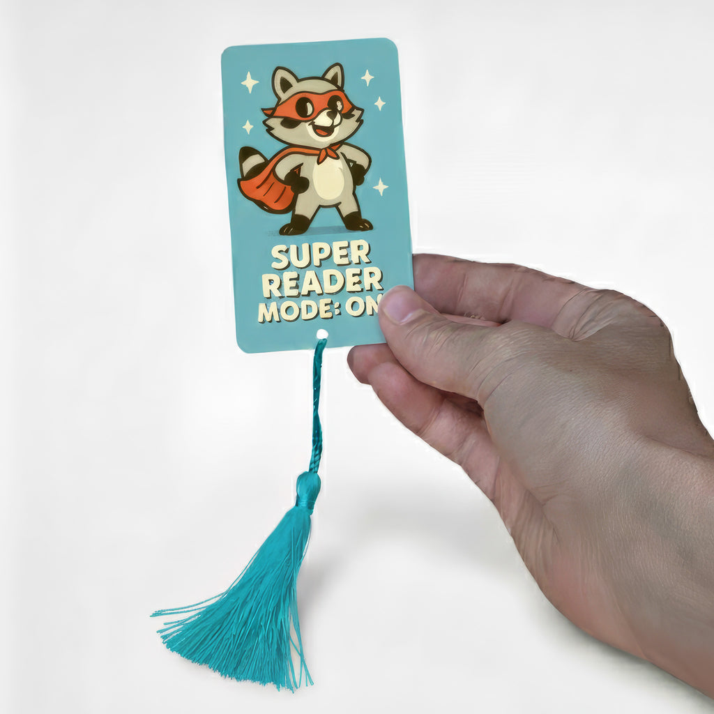 Personalised children’s bookmark featuring cartoon raccoon superhero wearing red cape and mask with text “Super Reader Mode: On” – custom metal bookmark for kids reading motivation, handmade in UK.