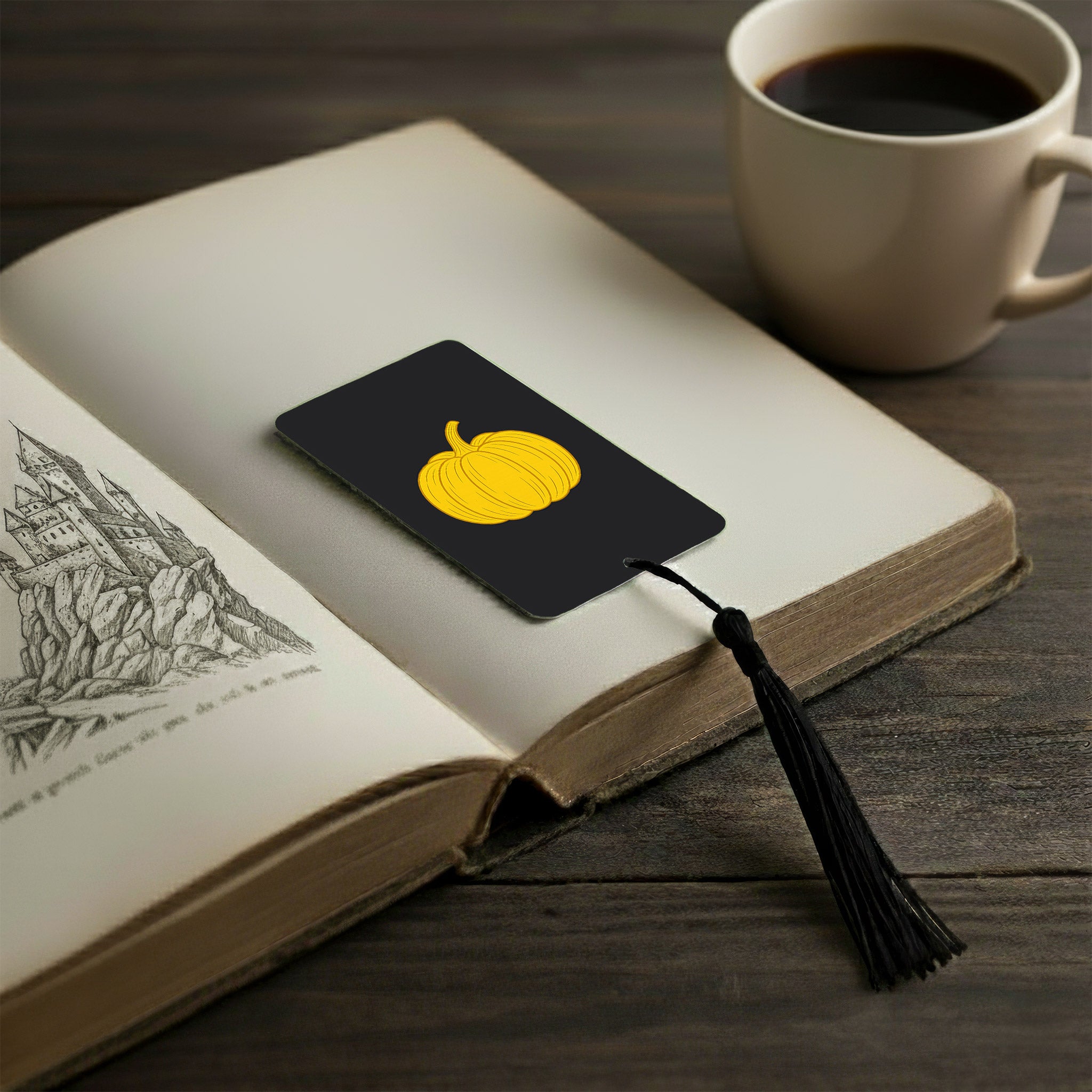 Black metal bookmark with yellow pumpkin design and matching black tassel placed in open book — cosy autumn aesthetic gift for readers, personalised metal bookmark UK.