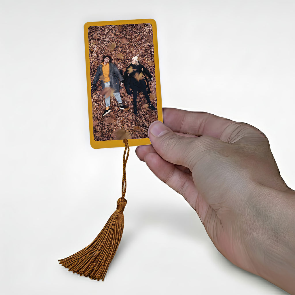 Hand holding personalised autumn photo bookmark with couple lying in autumn leaves — custom photo metal bookmark gift for readers, handmade in England.