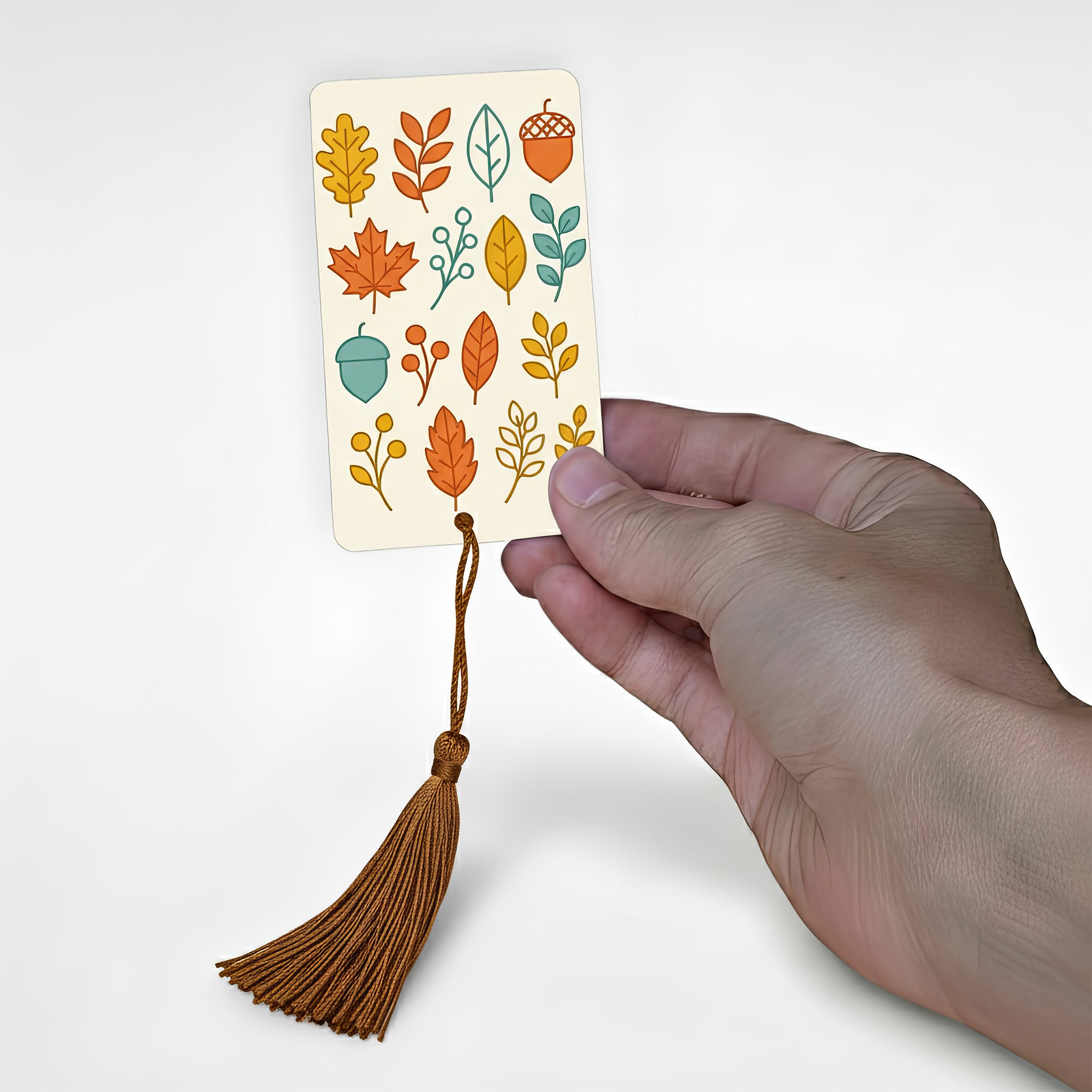 Hand holding minimalist autumn leaf pattern metal bookmark with golden brown tassel — stylish personalised autumn reading accessory made in Kent.