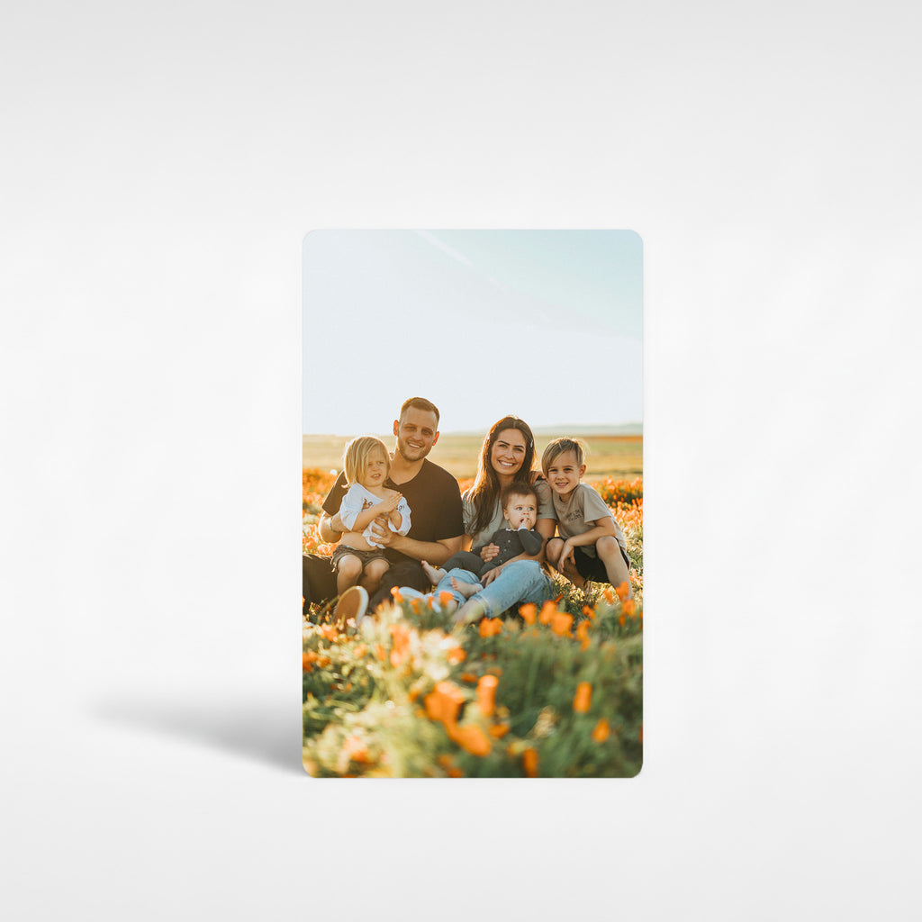 Personalised family photo fridge magnet showing a family sitting in a field of orange flowers, printed on glossy white aluminium.
