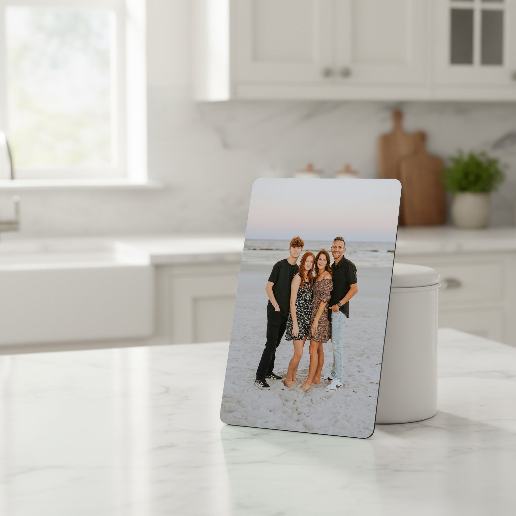 Personalised family photo fridge magnet printed on glossy white aluminium, displayed standing on a modern kitchen counter.