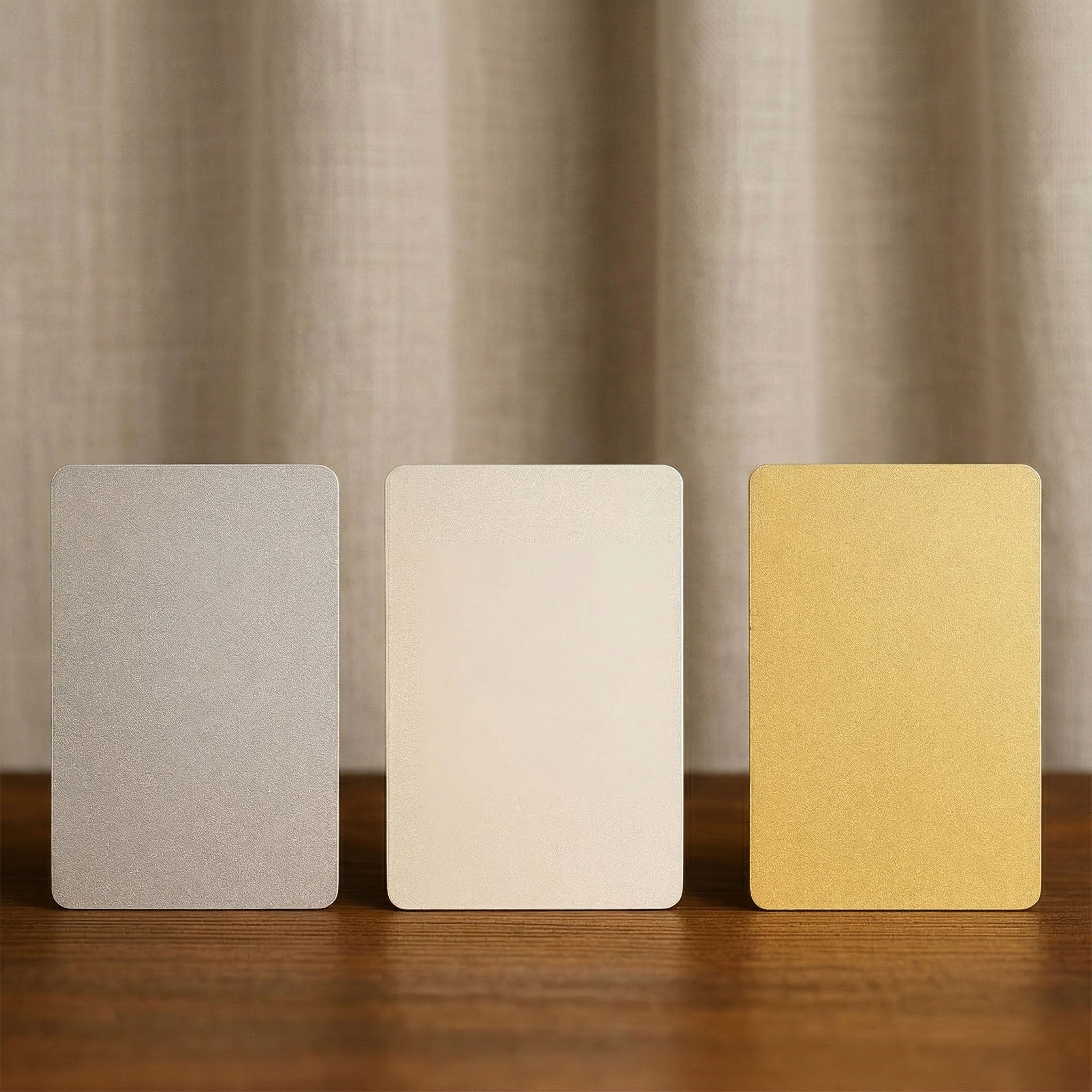 Three blank aluminium wallet cards standing upright, displaying the available finish options: brushed silver, standard white shimmer, and champagne gold.